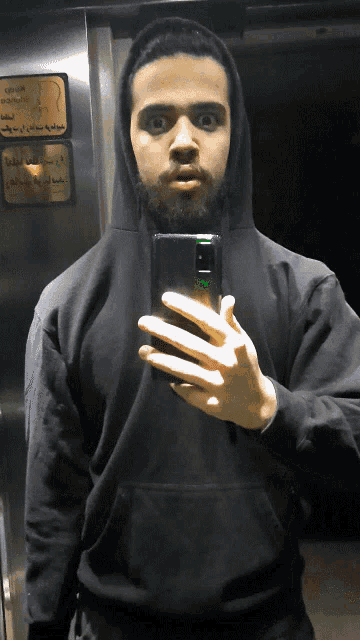 a man in a black hoodie takes a selfie in front of a sign that says ' elevator '