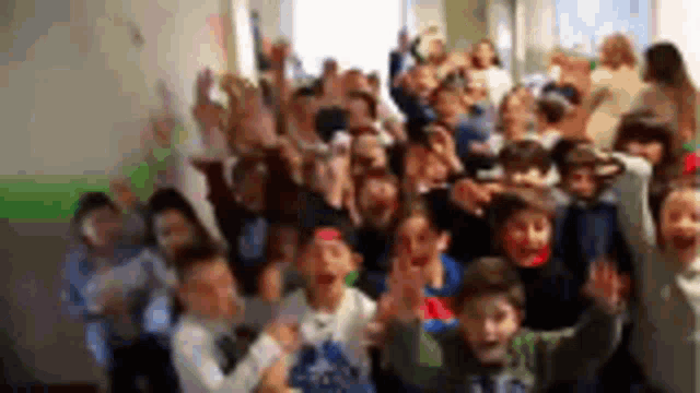 a large group of children are raising their hands in the air in a hallway .