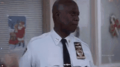 a police officer in a uniform and tie is standing in front of a window in a room .