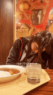 a woman is sitting at a table with a plate of curry and a glass of water