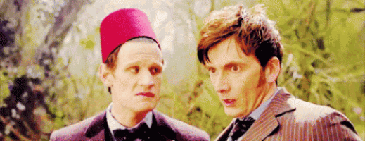 two men are standing next to each other and one of them is wearing a red hat and a suit .