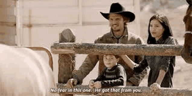 a man in a cowboy hat is standing next to a woman and a boy behind a fence .
