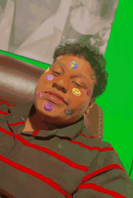 a man with smiley faces on his face is laying on a couch