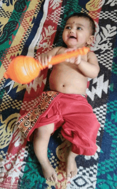 a baby is laying on a blanket holding an orange object