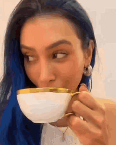 a woman with blue hair is drinking from a white and gold cup
