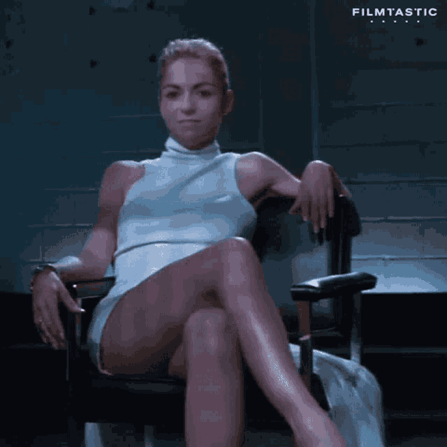 a woman in a white dress is sitting in a chair with her legs crossed and her hands on her knees .