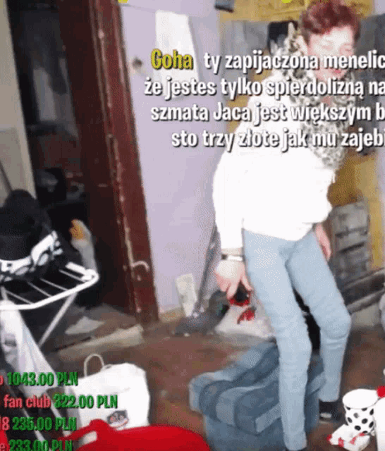 a woman standing in a messy room with a sign that says goha ty zapijaczona menolia