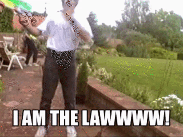 a man in a white shirt and black pants is holding a water gun and says i am the lawwww