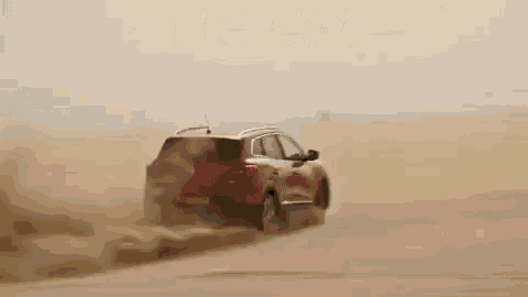 a red suv is driving through a desert .