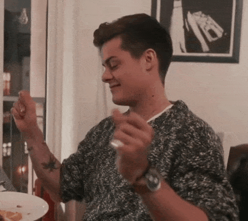 a young man is sitting at a table with a plate of food in front of him and dancing .