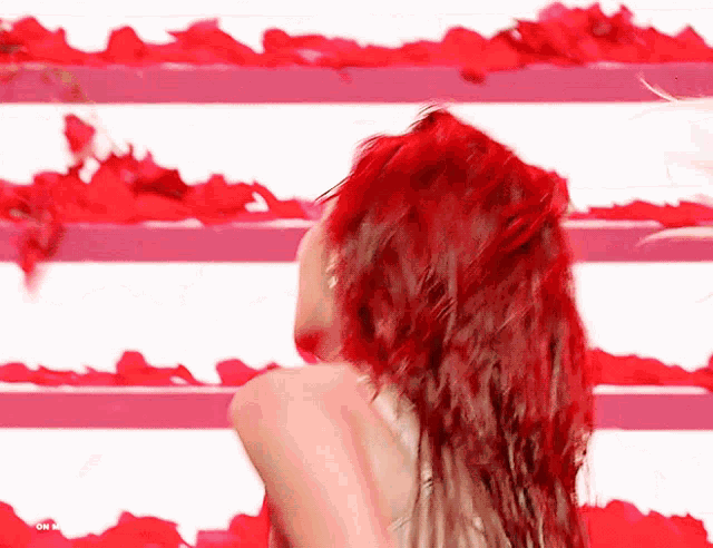 a woman with red hair is standing in front of a wall of red petals
