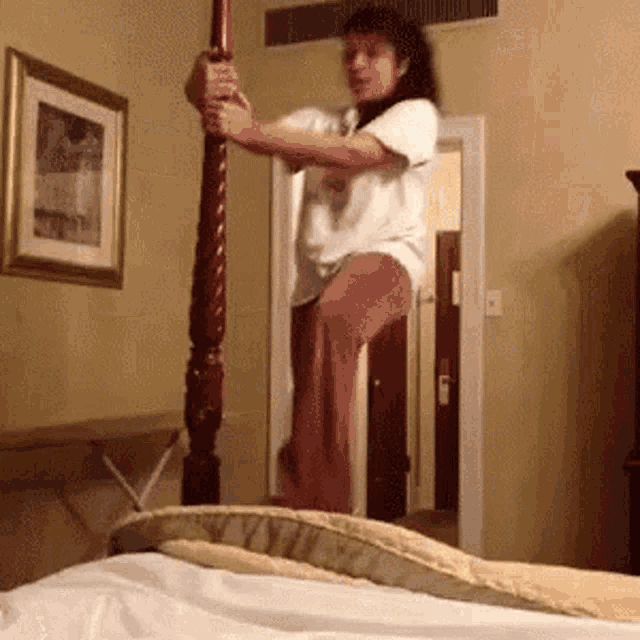 a woman in a white shirt is standing on a bed holding a pole
