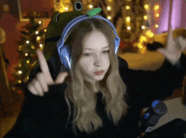 a girl wearing a frog hat and headphones is giving the middle finger