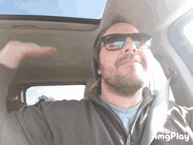 a man wearing sunglasses and a beanie is in a car with imgplay written on the bottom