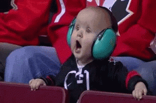 a baby wearing headphones is sitting in a stadium with his mouth open .