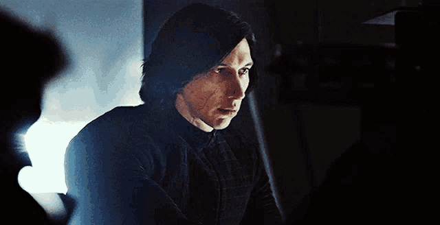 a man with long hair is sitting in a dark room looking at something .