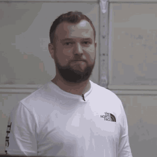 a man with a beard is wearing a white north face t-shirt
