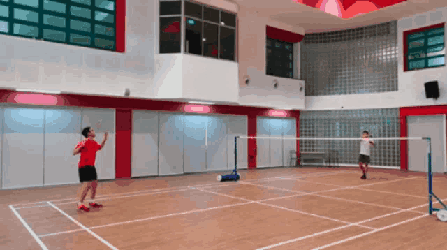 a man in a red shirt is playing badminton with another man