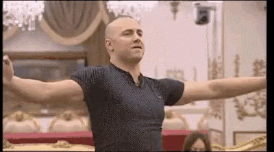 a bald man in a blue shirt is standing with his arms outstretched in a room .