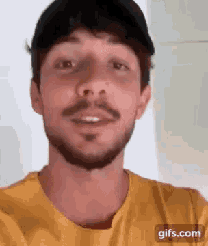 a man with a beard and a yellow shirt is wearing a black hat .