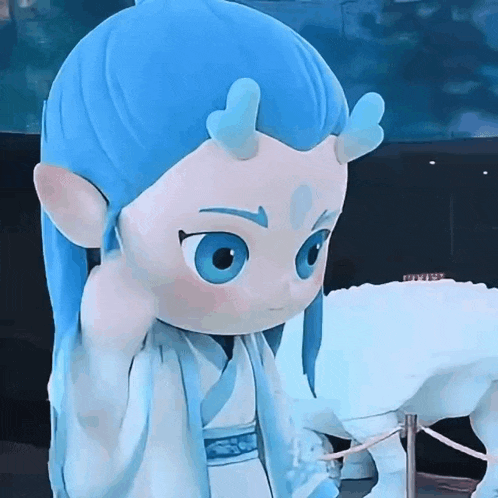 a stuffed animal with blue hair and horns is standing next to a statue of a dragon .