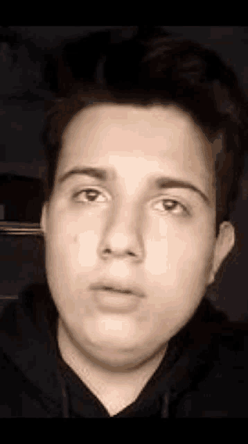 a young man wearing a black hoodie is looking at the camera .