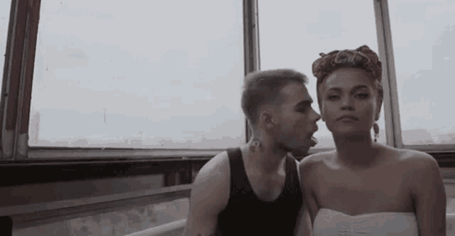 a man is kissing a woman on the cheek while they are sitting next to each other in front of a window .