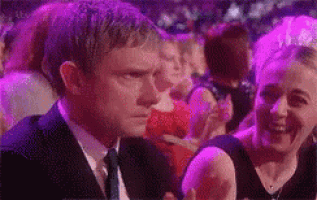 a man in a suit and tie is sitting in a crowd of people with purple lights .