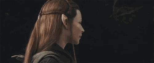 a woman with long red hair and elf ears is standing in the dark and looking at the camera .