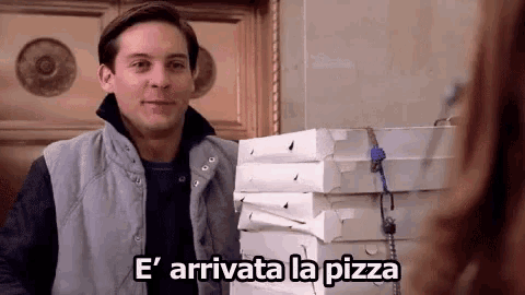 a man in a vest is standing next to a pile of pizza boxes and says e ' arrivata la pizza .