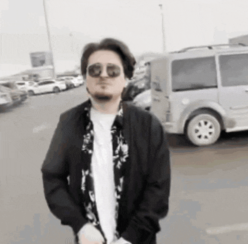 a man wearing sunglasses and a black jacket is standing in front of a van .