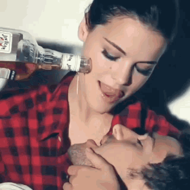 a woman is pouring a bottle of jack daniels into a man 's mouth .