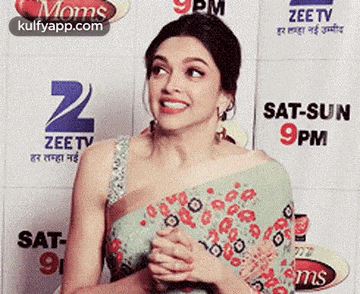 a woman in a saree is standing in front of a wall with a zee tv logo .