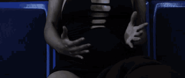 a woman in a black dress is sitting in a blue chair with her hands on her stomach