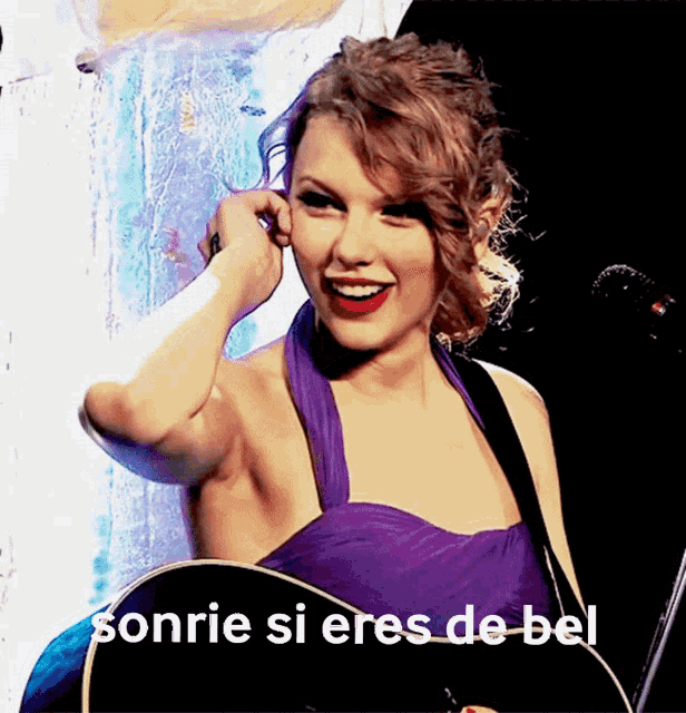 a woman in a purple dress is smiling while holding a guitar and the words sonrie si eres de bel are above her