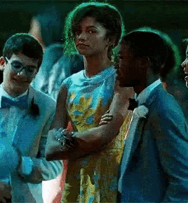 a woman in a yellow dress is standing next to two men in tuxedos at a prom .
