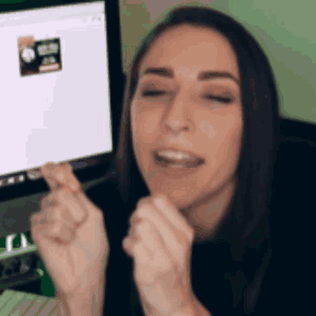 a woman is sitting in front of a computer and making a heart shape with her hands .