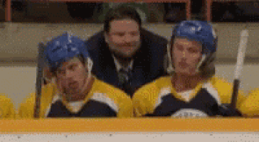 a group of hockey players sitting in the stands with a referee behind them .