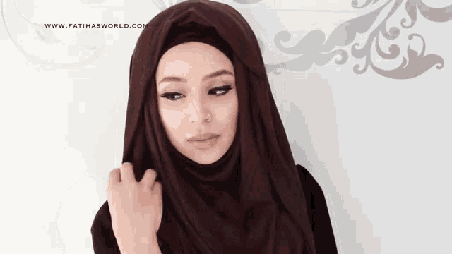 a woman wearing a hijab is standing in front of a wall .