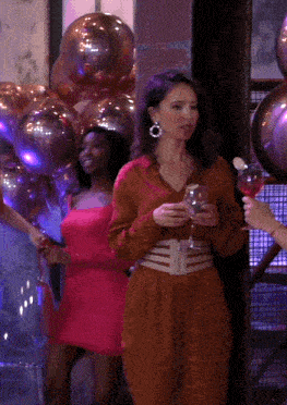 a woman in a brown dress holds a glass of wine in front of balloons