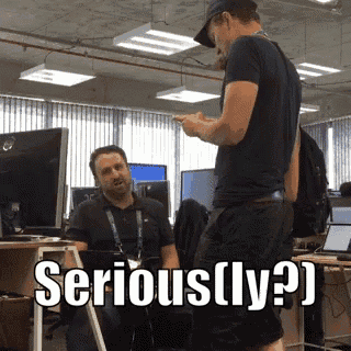 a man standing next to a man sitting at a desk with the words serious ( ly ) written on it