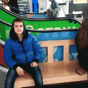 a young man in a blue jacket is sitting on a bench in front of an escalator