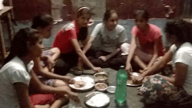 a group of girls are sitting around a table with plates of food and a green bottle