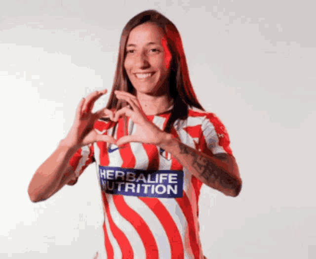 a woman wearing a red white and blue shirt that says herbalife nutrition makes a heart shape with her hands