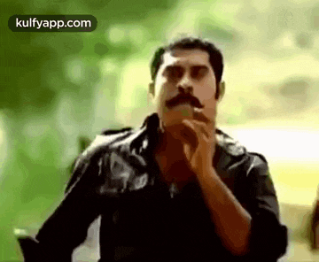 a man with a mustache is smoking a cigarette in front of a green background .