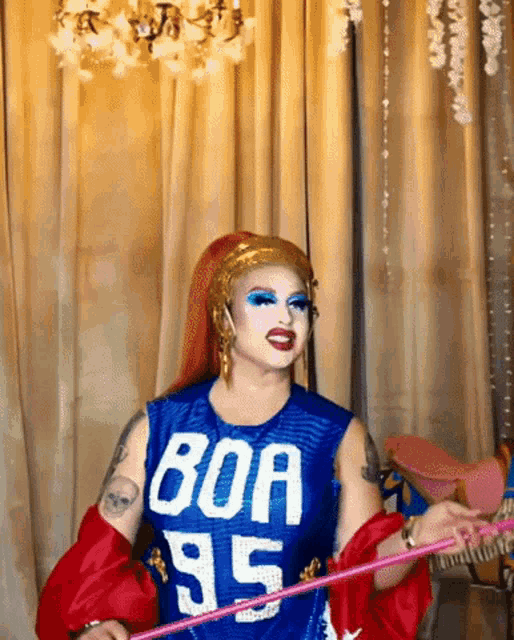 a drag queen is wearing a blue boa 95 shirt