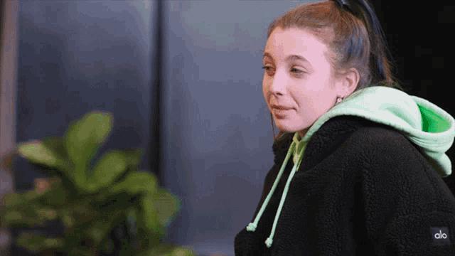 a woman wearing a black and green hoodie with the word alo on the back
