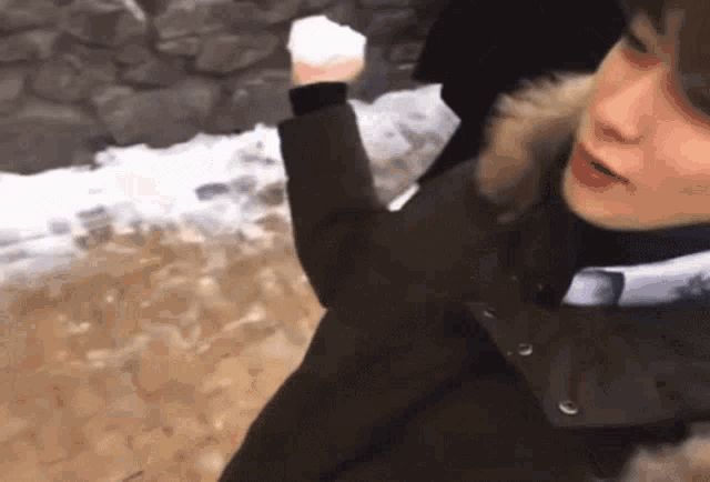 a person wearing a fur hooded jacket holds a snowball in their hand