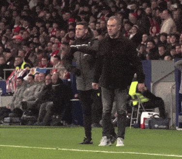 a man in a black jacket with the letter o on it stands on a soccer field