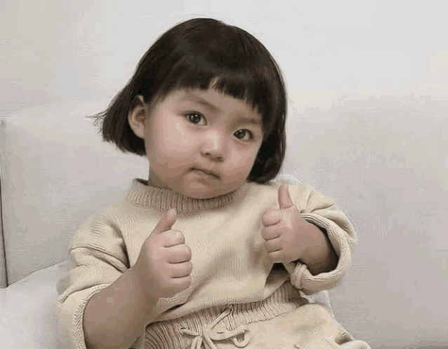 a little girl is sitting on a couch and giving a thumbs up .